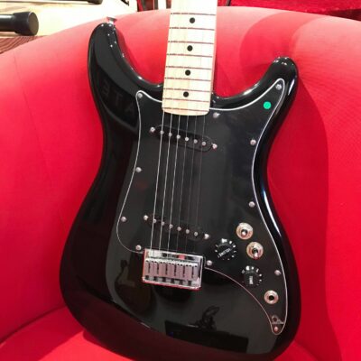 guitare électrique noire posée sur fauteuil rouge