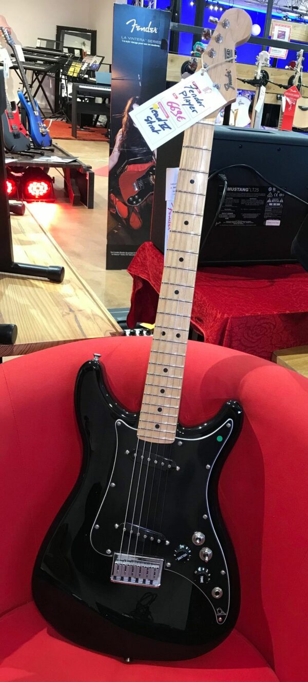 guitare électrique noire posée sur fauteuil rouge
